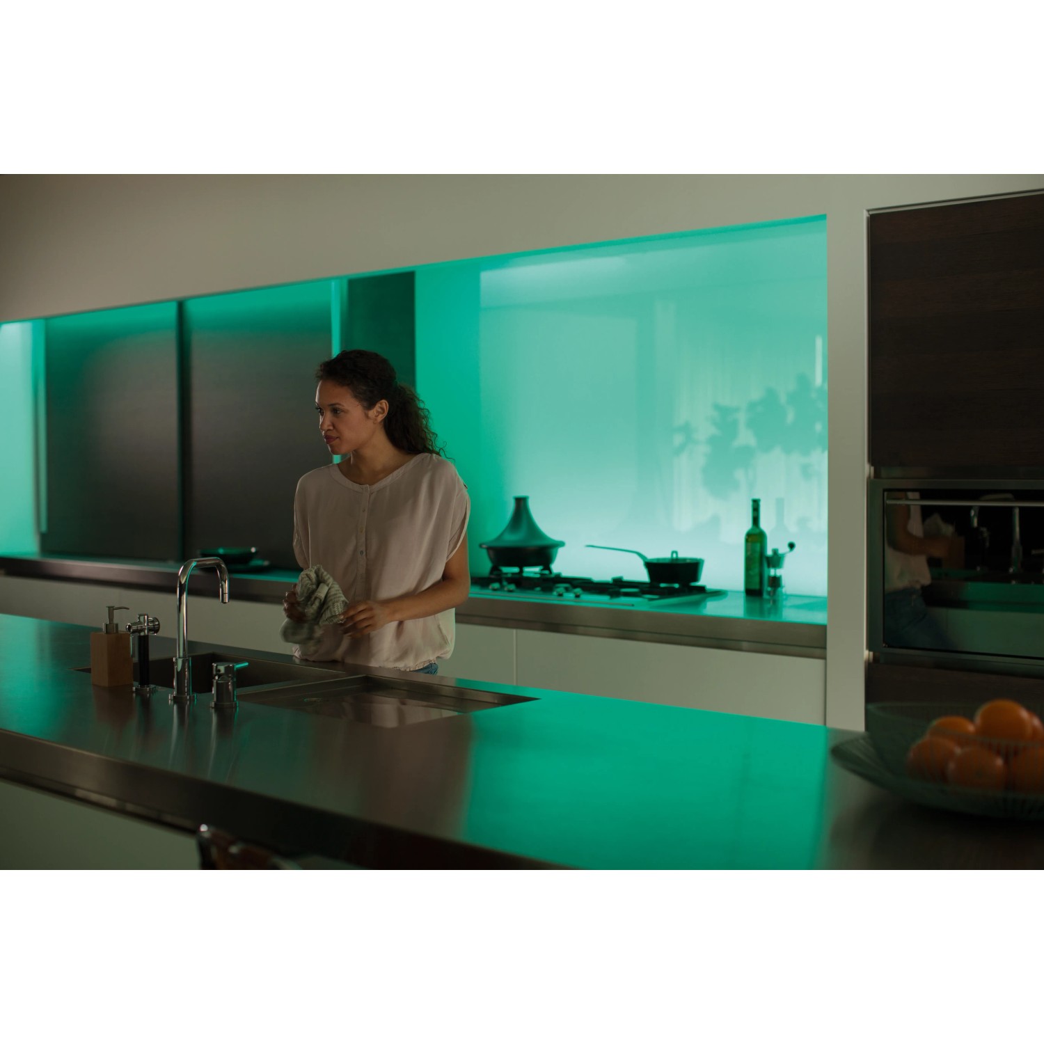 Frau in Küche mit Philips Hue Lightstrip Plus, der grünes Licht ausstrahlt.