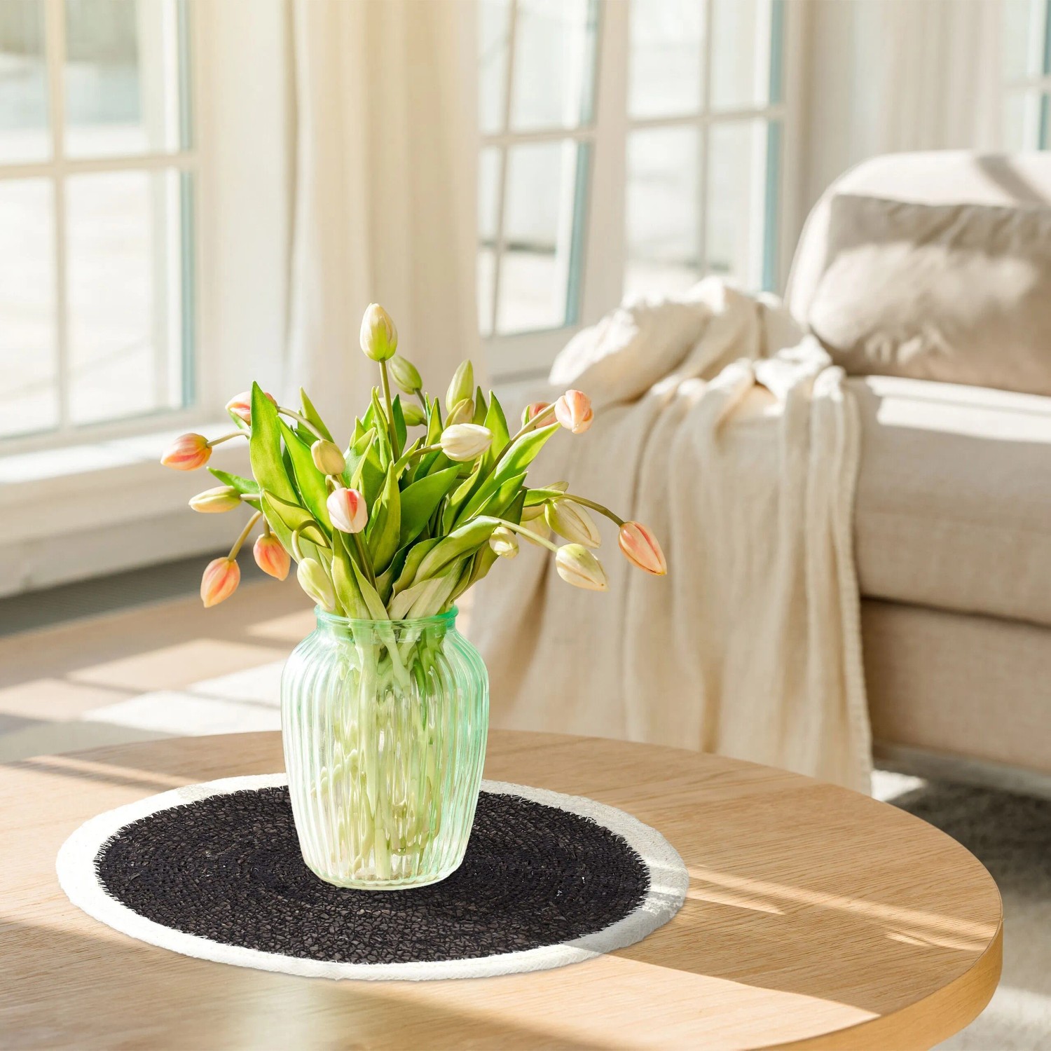 Rundes Tischset aus geflochtenem Seegras in Schwarz und Creme auf Holztisch mit Blumenvase.