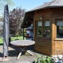 Graue Perel Schutzhülle für Gartenschirm, stehend auf Terrasse neben Holztisch und Gartenhaus.