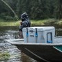 Dunkelgraue Kühlbox aus Kunststoff auf einem Boot, mit Angler im Hintergrund. Ideal für Outdoor-Aktivitäten.
