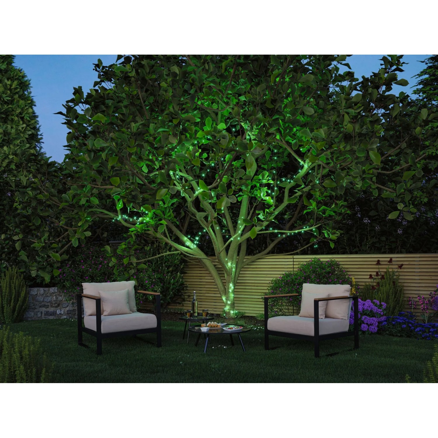 Paulmann LED-Lichterkette Yuna RGB leuchtet grün am Baum in einem Garten mit Sitzgruppe.