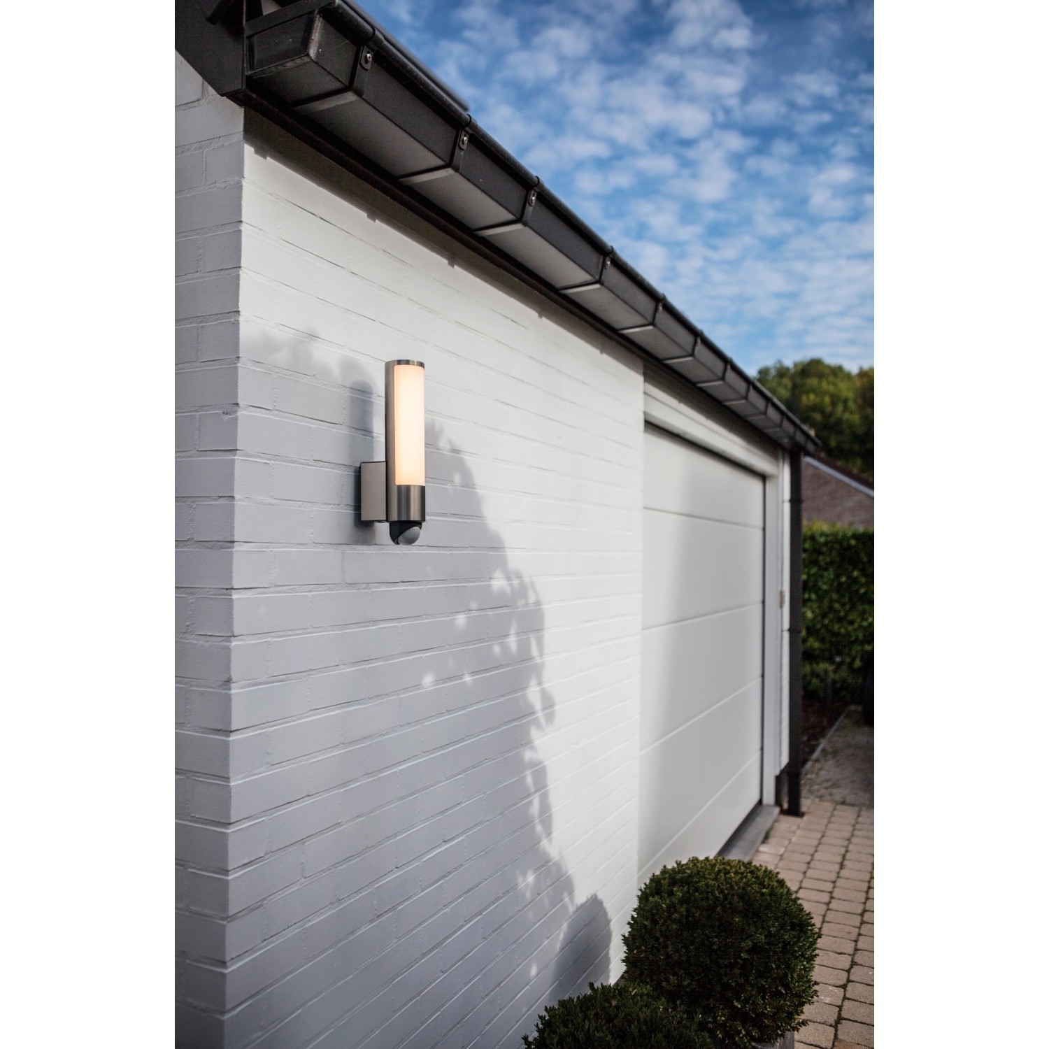 Moderne Lutec LED-Außenwandleuchte Leda mit Bewegungsmelder an weißer Hauswand.