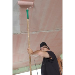 Mann trägt Knauf Betokontakt Haftgrund mit Farbroller auf Decke auf.