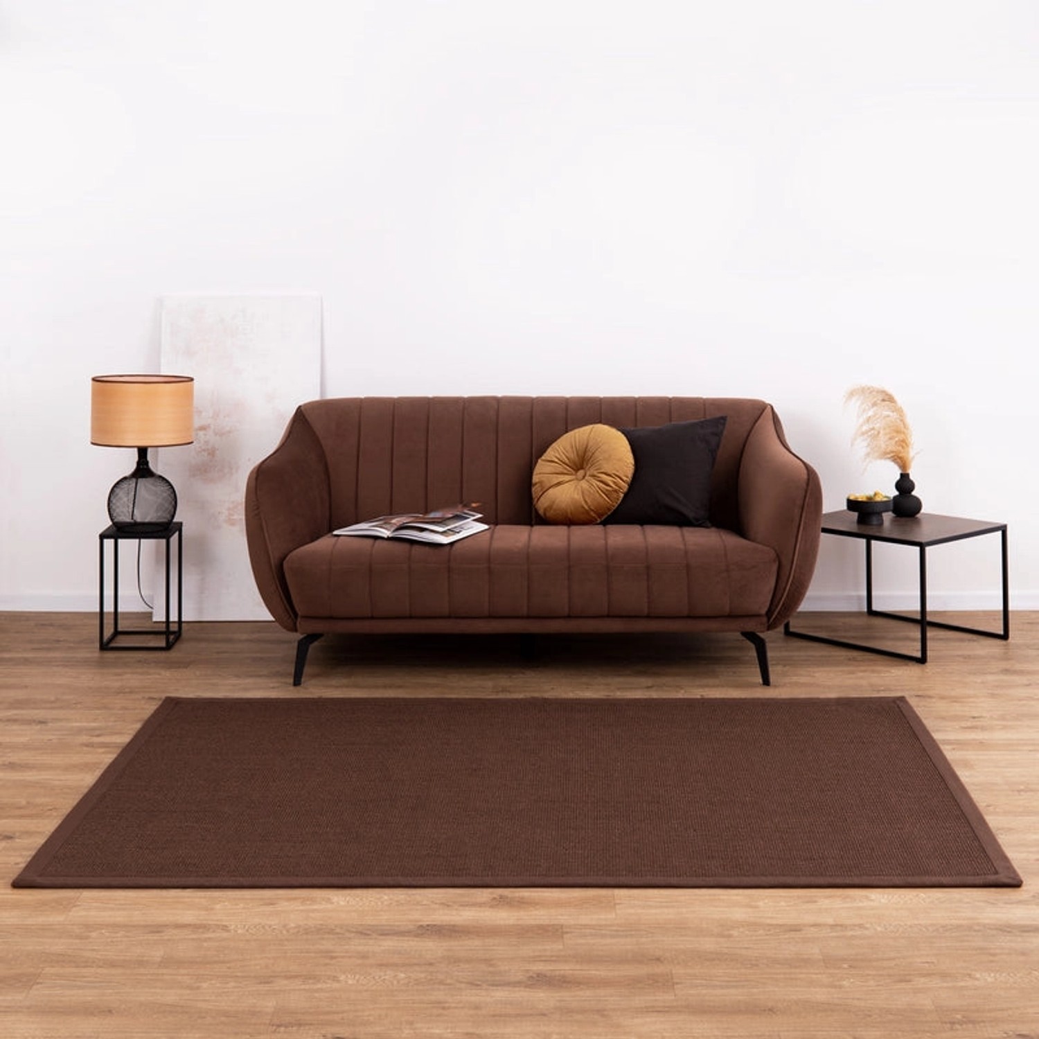 Dunkelbrauner KARAT Sisalteppich Amazonas mit breiter Bordüre, passend zu Wohnbereich mit Sofa.