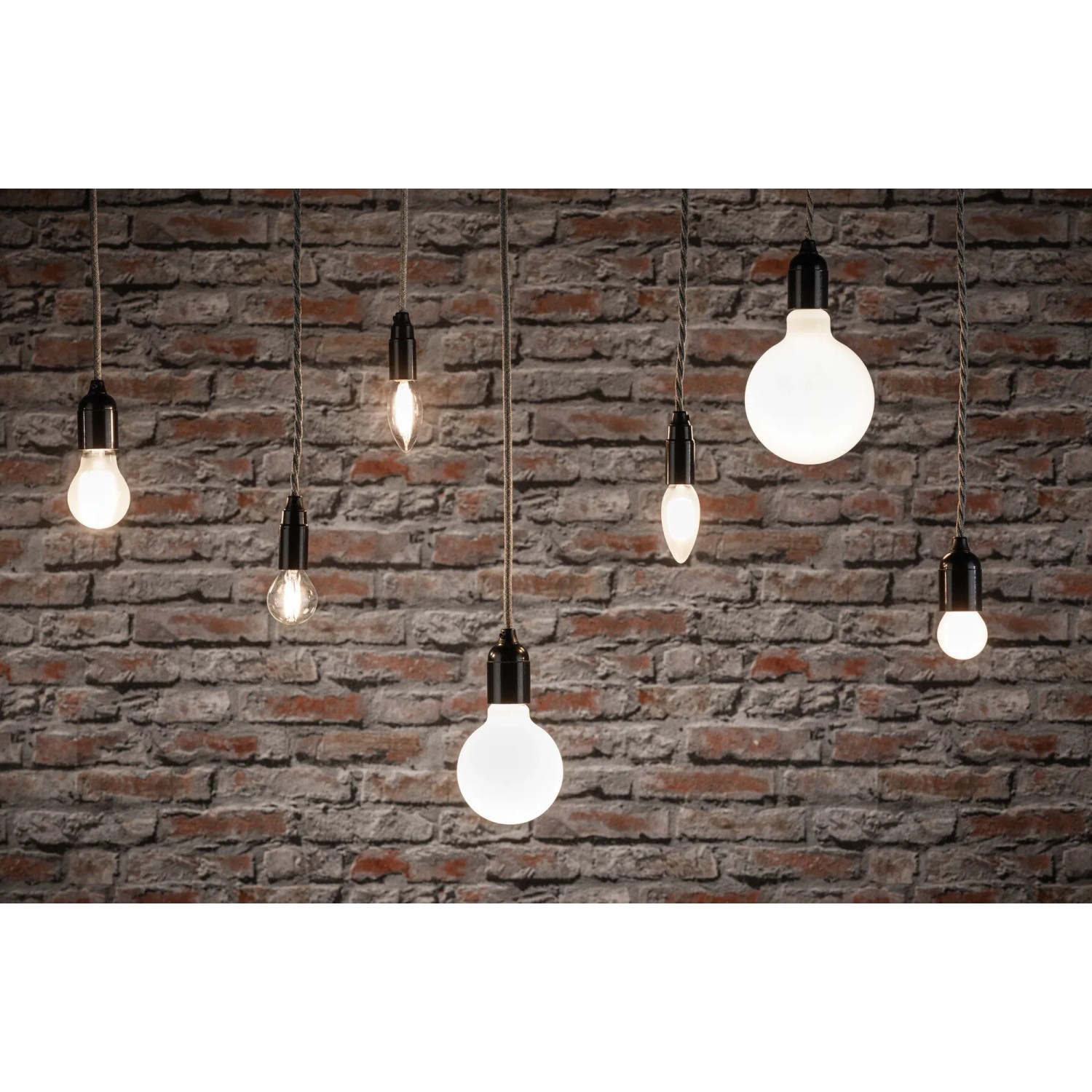 Verschiedene Paulmann E14 LED Leuchtmittel in Tropfenform vor einer Backsteinwand.