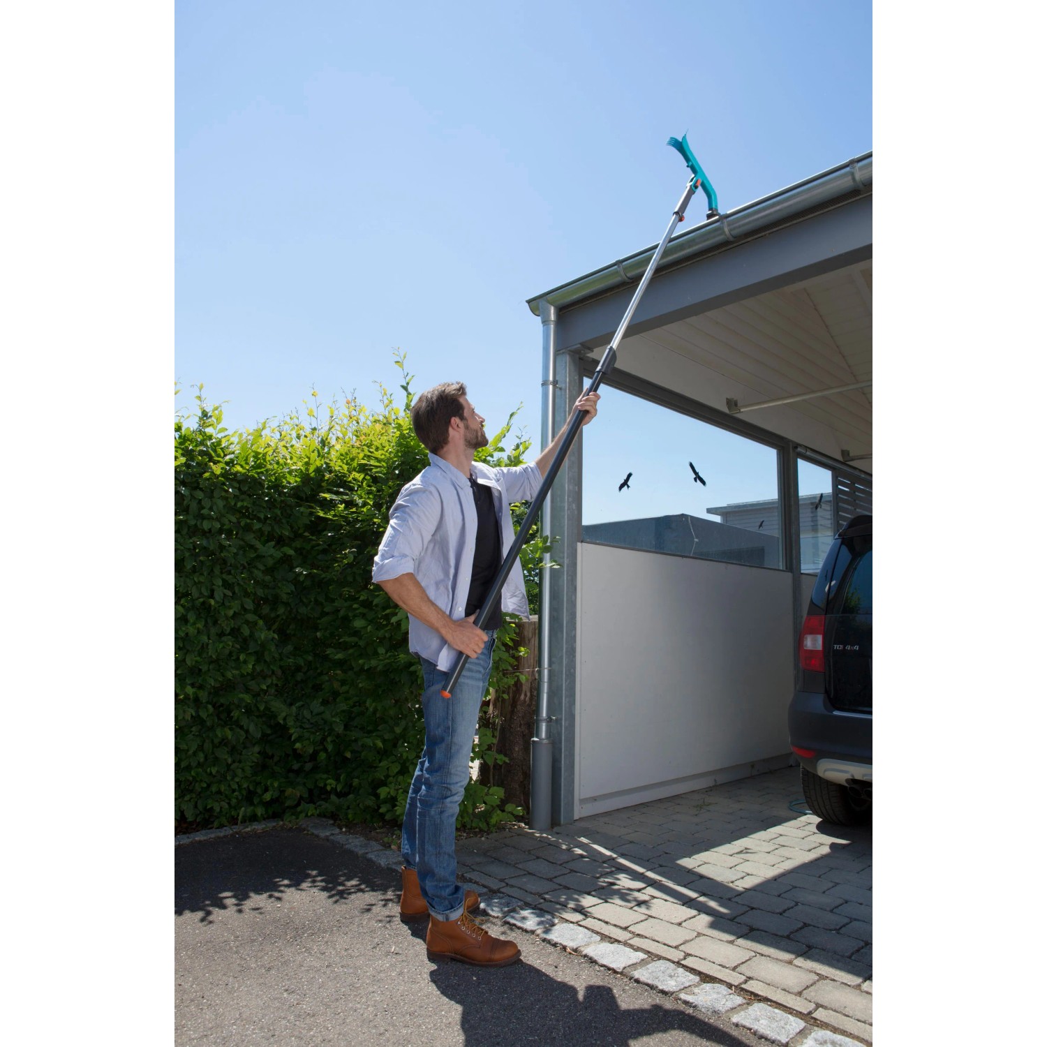 Mann reinigt Dachrinne mit Gardena combisystem-Dachrinnenreiniger und Teleskopstiel.