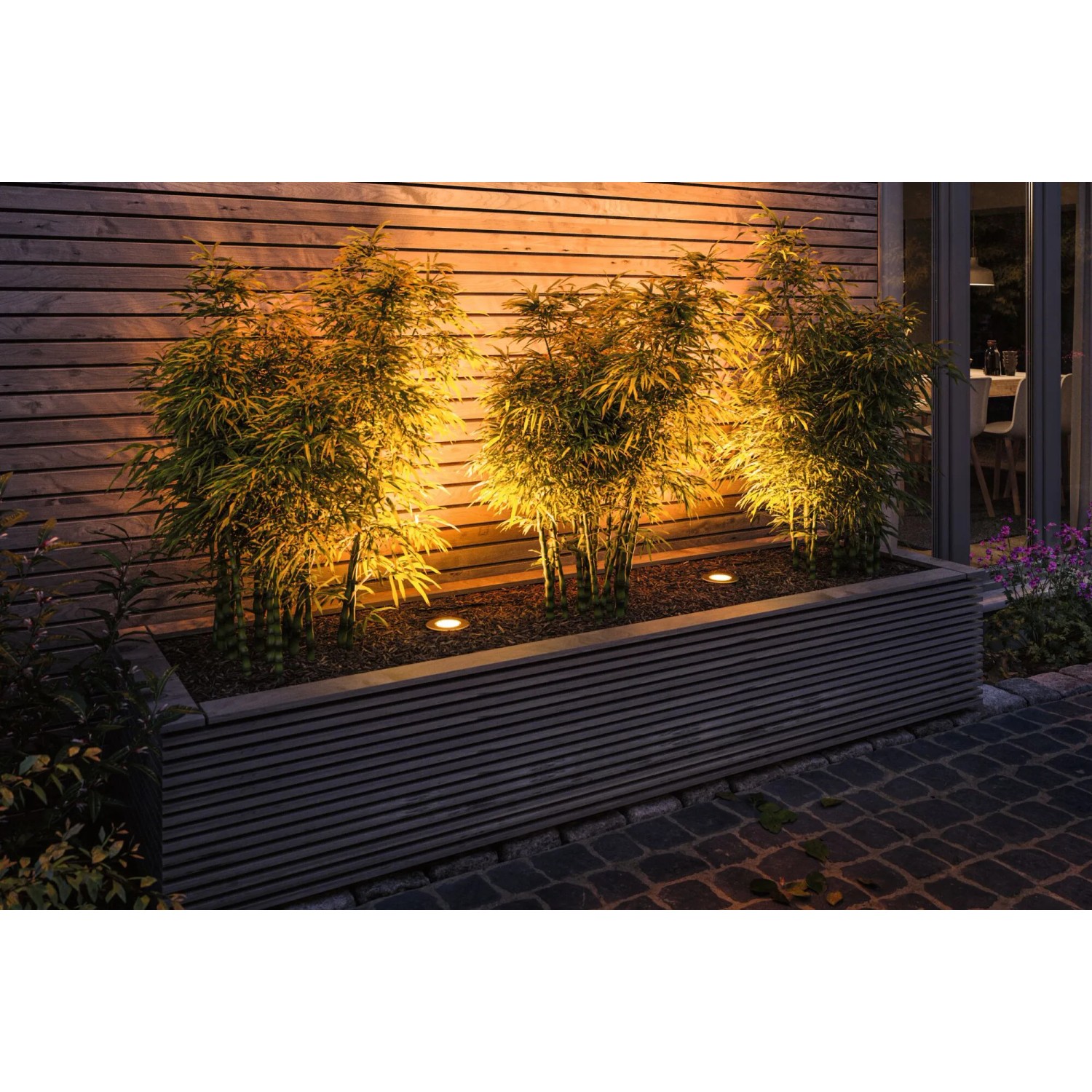 Paulmann Outdoor-Bodeneinbaustrahler Floor Edelstahl, rund, beleuchtet Pflanzen in einem Beet.
