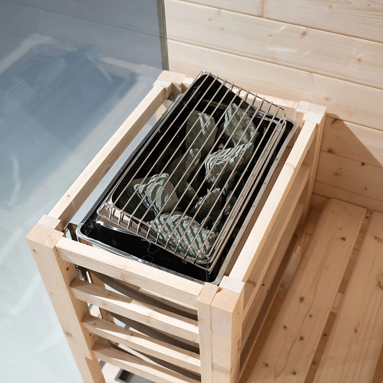 Saunaofen mit Saunasteinen der Home Deluxe SHADOW M Sauna aus hellem Holz.