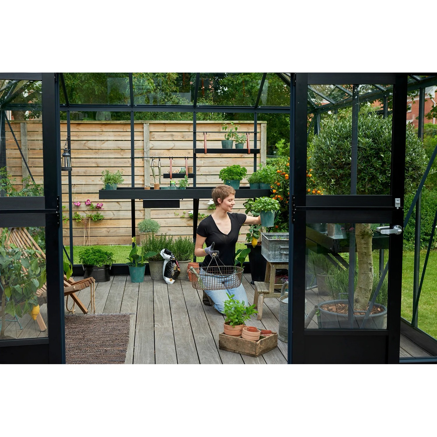 Juliana Gewächshaus Oase 13 Anthrazit mit Frau und Pflanzen im Garten.