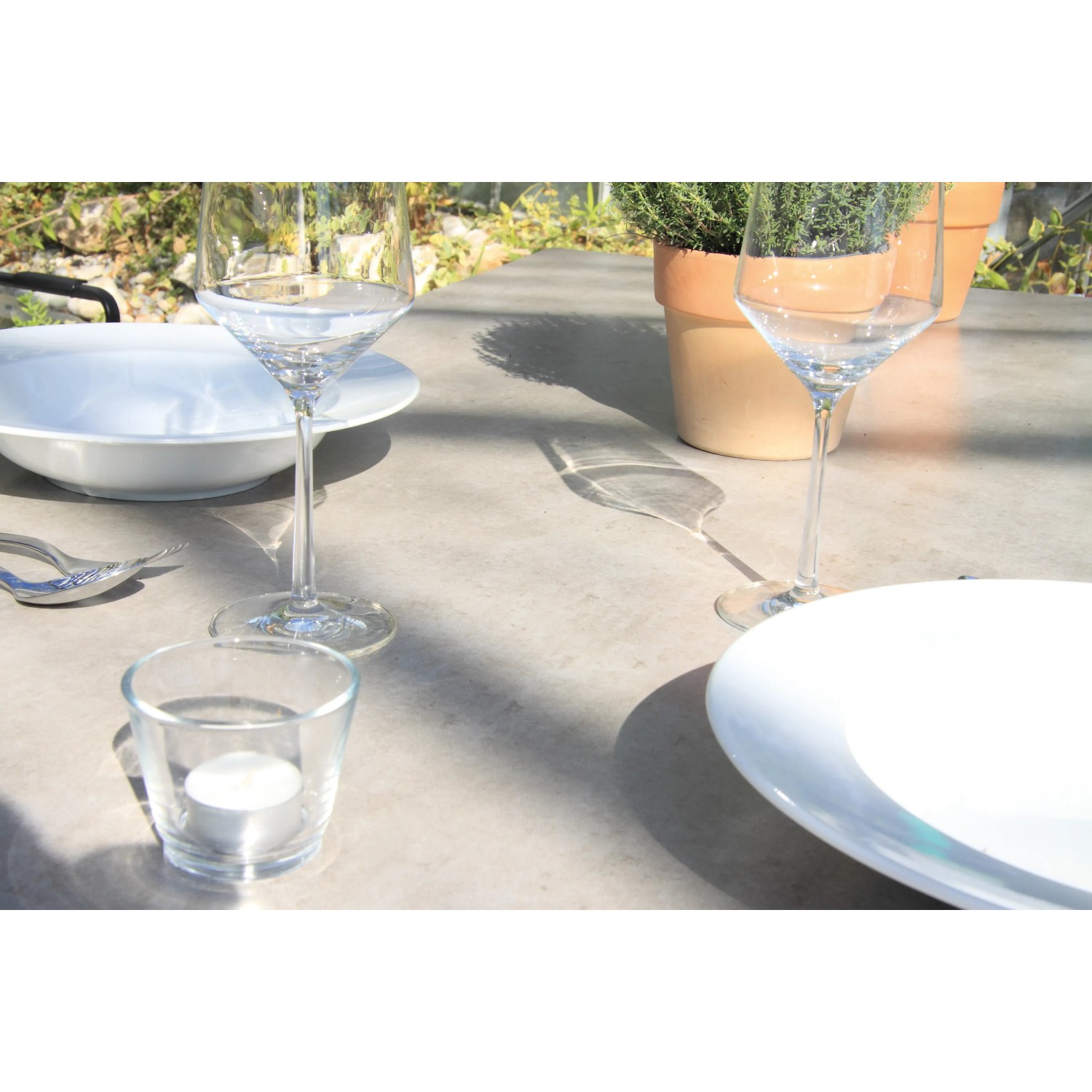 Detailansicht des Acamp Gartentisch Alpha Cemento mit Gläsern und Geschirr.