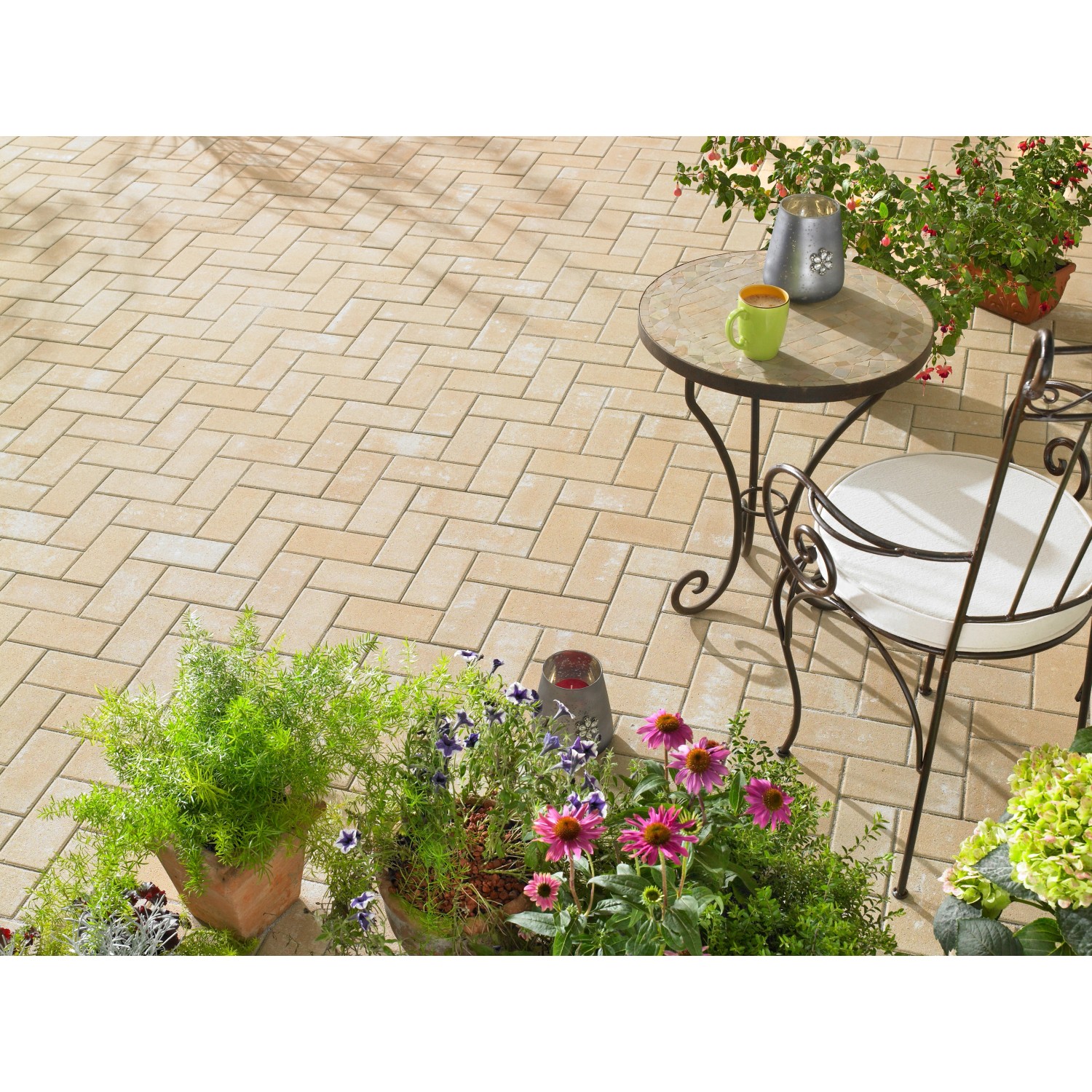 Verlegtes Rechteck-Pflaster Beton Sandstein (20x10x6 cm) auf einer Terrasse mit Gartenmöbeln und Pflanzen.