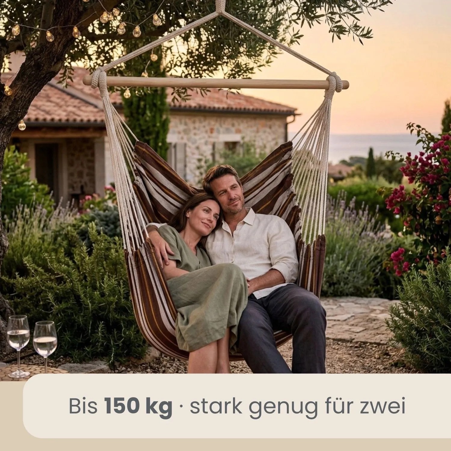 Gestreifter AMANKA Hängesessel mit Paar im Garten. 150 kg belastbar, aus Baumwolle, mit Holzstab. Gemütlicher Schwebesessel für draußen.