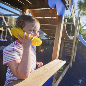 Mädchen telefoniert im Wickey Sandkasten King Kong mit gelbem Spielzeug. Sandkasten mit Deckel im Garten.