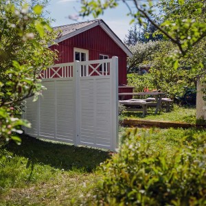 Weißer Sichtschutzzaun Nostalgi aus Nadelholz (90x180cm) vor rotem Gartenhaus im Grünen.