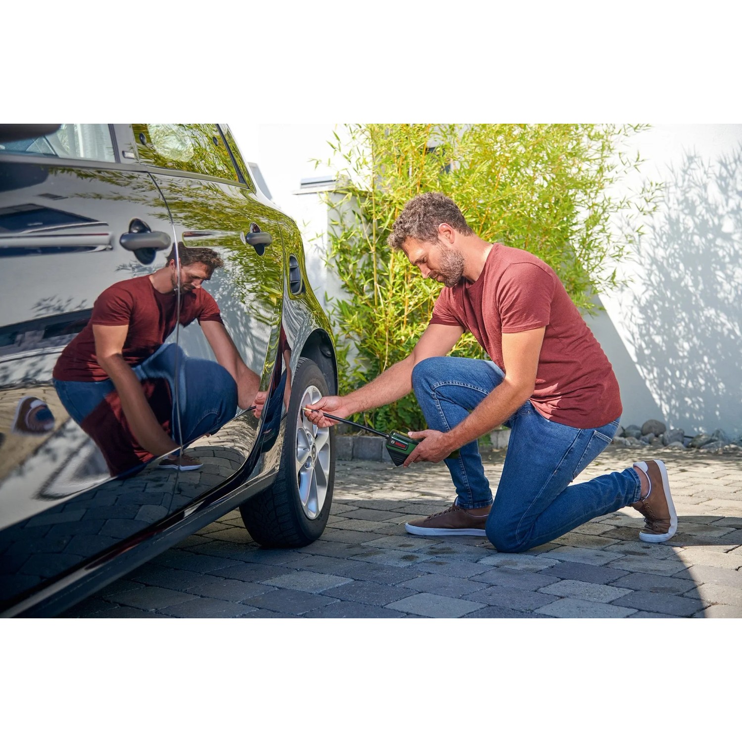 Mann pumpt Autoreifen mit Bosch Akku-Druckluftpumpe Pneo auf.