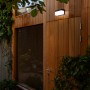 Schwarze, eckige Lutec LED Solar Wandleuchte Fran an einer Holzwand. Moderne Außenleuchte mit Bewegungsmelder.