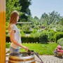 Gardena Akku-Regenfasspumpe 2000/2: Frau bedient Pumpe am Fass, Gartenbewässerung im Hintergrund.