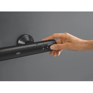 Schwarze Grohe Precision Flow Thermostat-Duscharmatur, matt, an dunkler Wand. Eine Hand stellt die Temperatur auf 38°C ein.