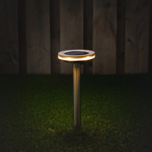 Graue Solarleuchte Johannesburg mit Erdspieß im Garten, leuchtet warmweiß.