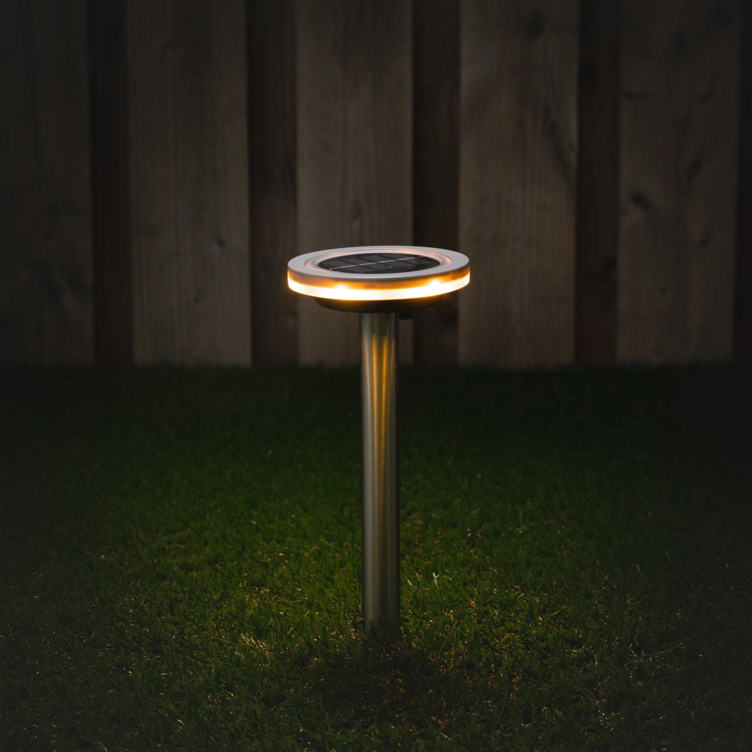 Graue Solarleuchte Johannesburg mit Erdspieß im Garten, leuchtet warmweiß.
