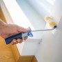 Hand streicht Wand mit LUX Dispersionswalze 12 cm. Farbwalze mit blau-grauem Griff.