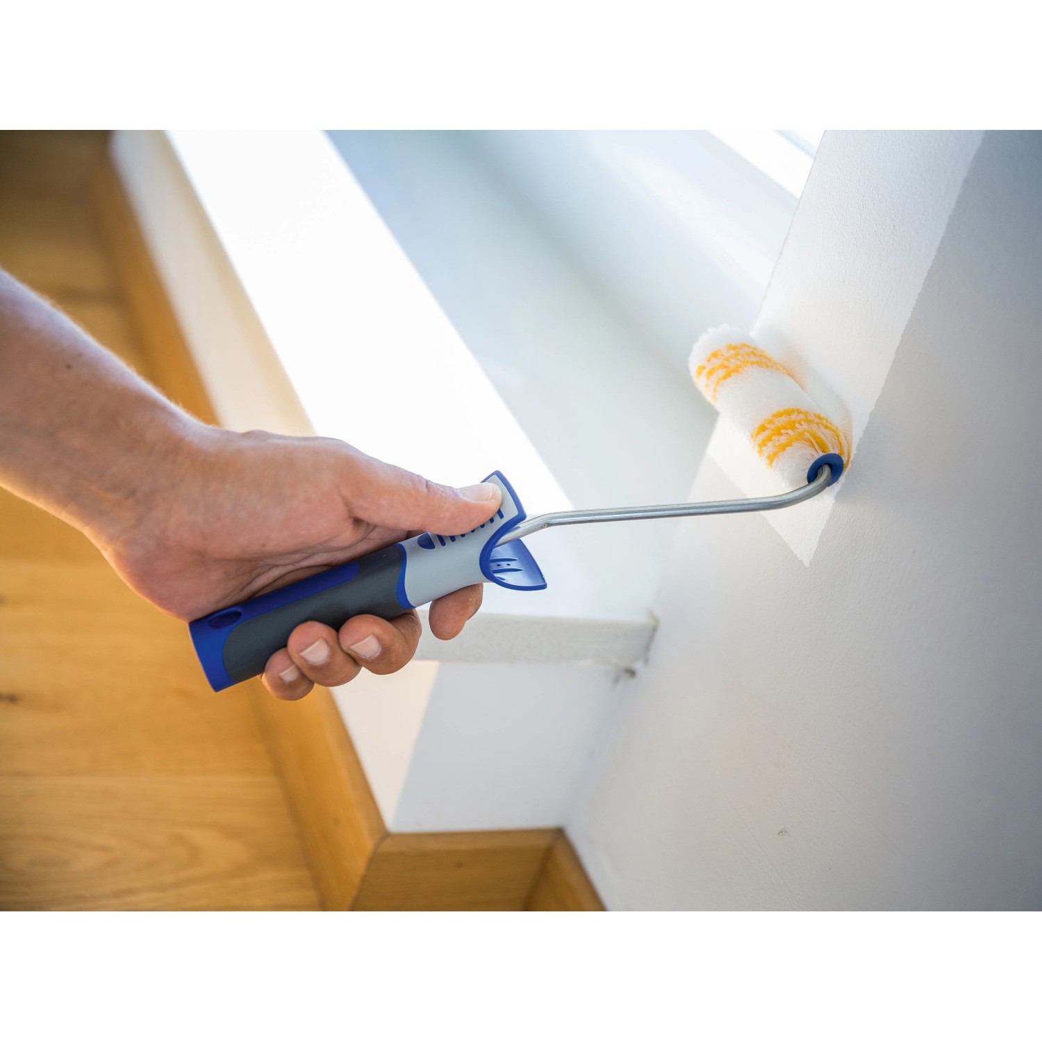 Hand streicht Wand mit LUX Dispersionswalze 12 cm. Farbwalze mit blau-grauem Griff.