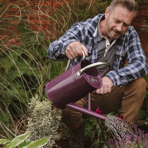 Mann gießt mit violetter Kent & Stowe Gießkanne Blumen im Garten.