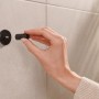 Montage eines schwarzen, matten Tesa Handtuchhakens Moon mit Klebelösung an einer gefliesten Wand.