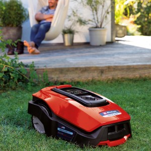 Roter Einhell Freelexo 600 Mähroboter auf Rasen, Mann entspannt in Hängematte im Hintergrund.