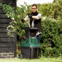 Frau bedient Bosch Gartenhäcksler AXT 25 TC. Elektro-Häcksler zerkleinert Äste im Garten.
