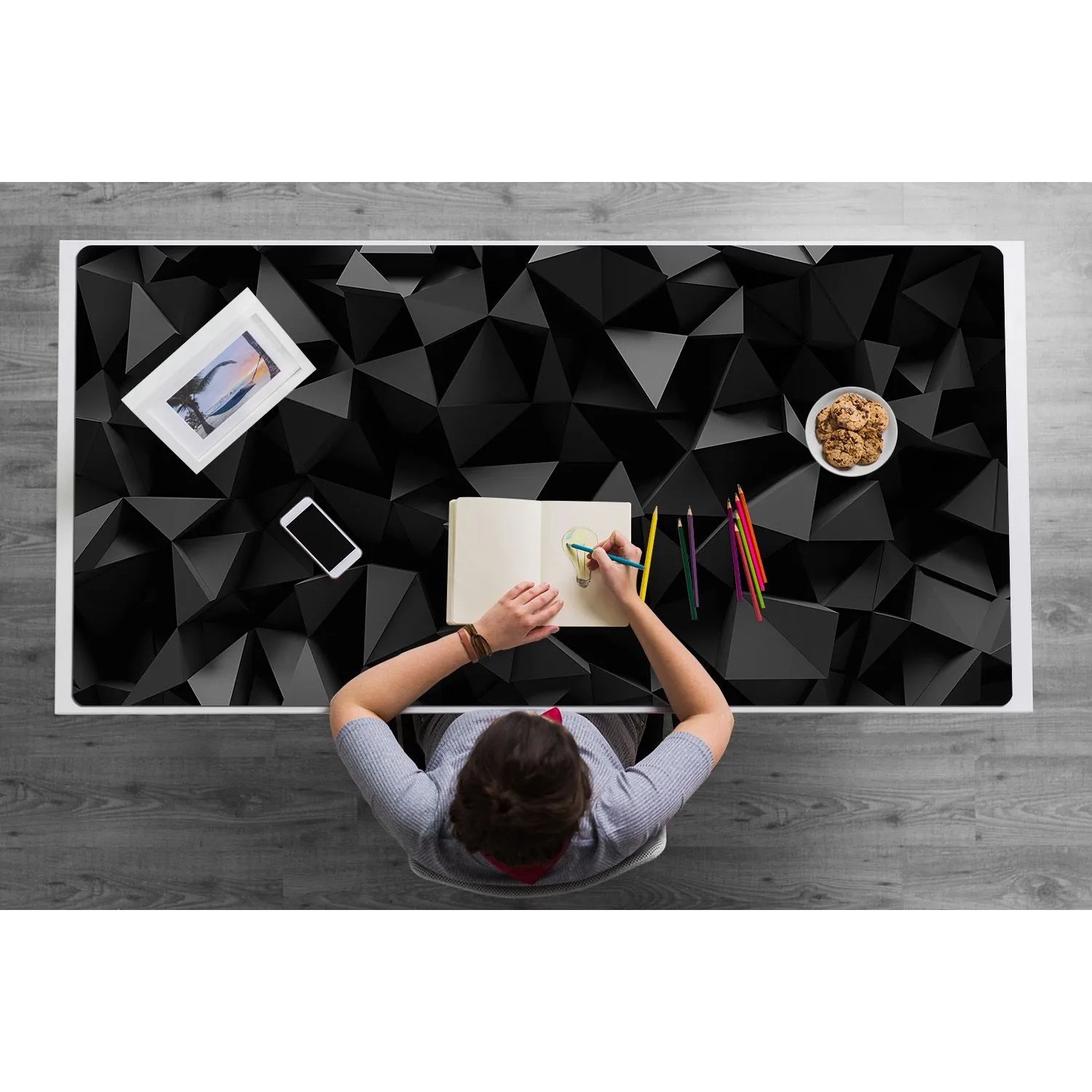 Schwarze Schreibtischunterlage mit abstraktem 3D-Muster auf weißem Schreibtisch, Person zeichnet. Ideal für Büro & Homeoffice.