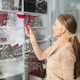 Frau reinigt Fenster mit Vileda Profi-Fensterwischer Handgerät. Reinigungsgerät mit rotem Griff.