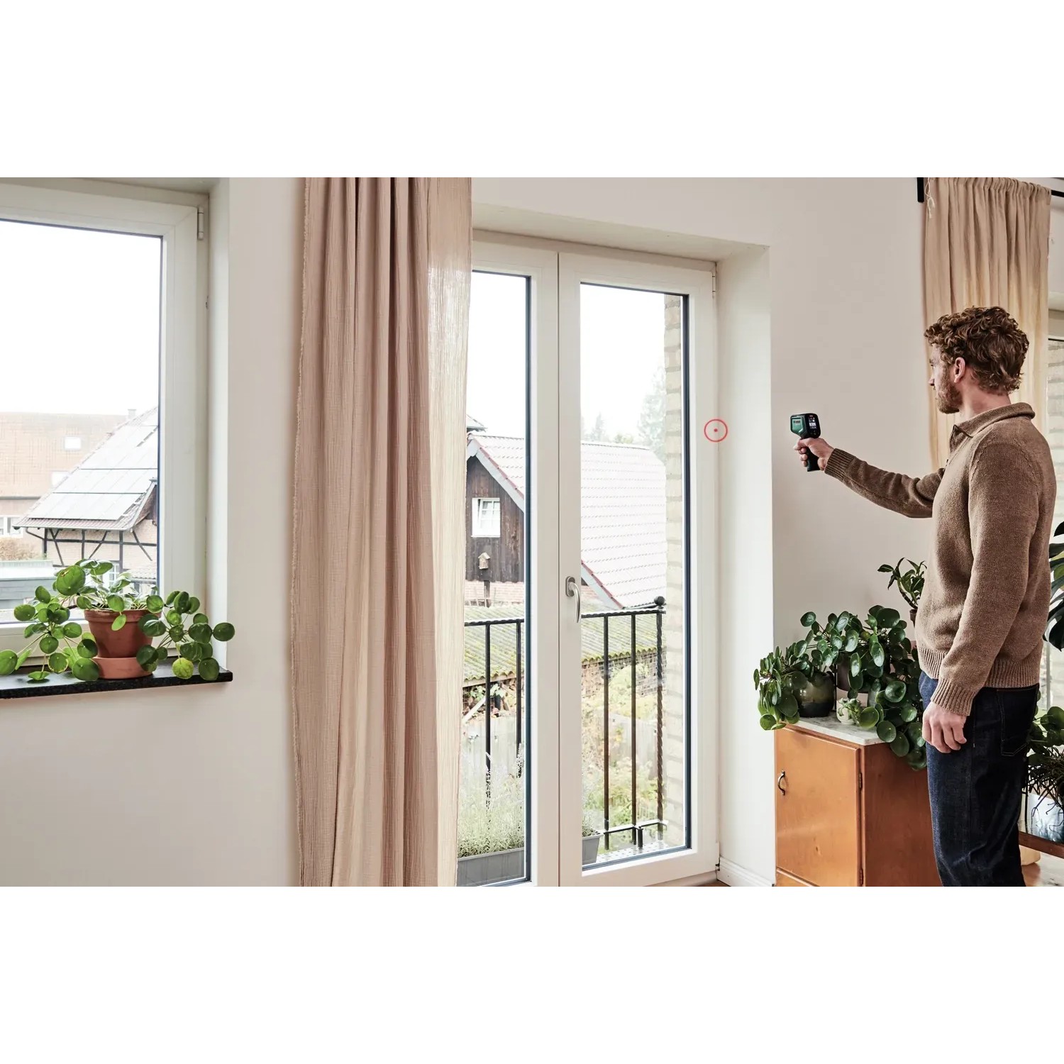 Mann misst mit dem Bosch AdvancedTemp Infrarot-Thermometer die Temperatur an einer Wand im Innenraum.