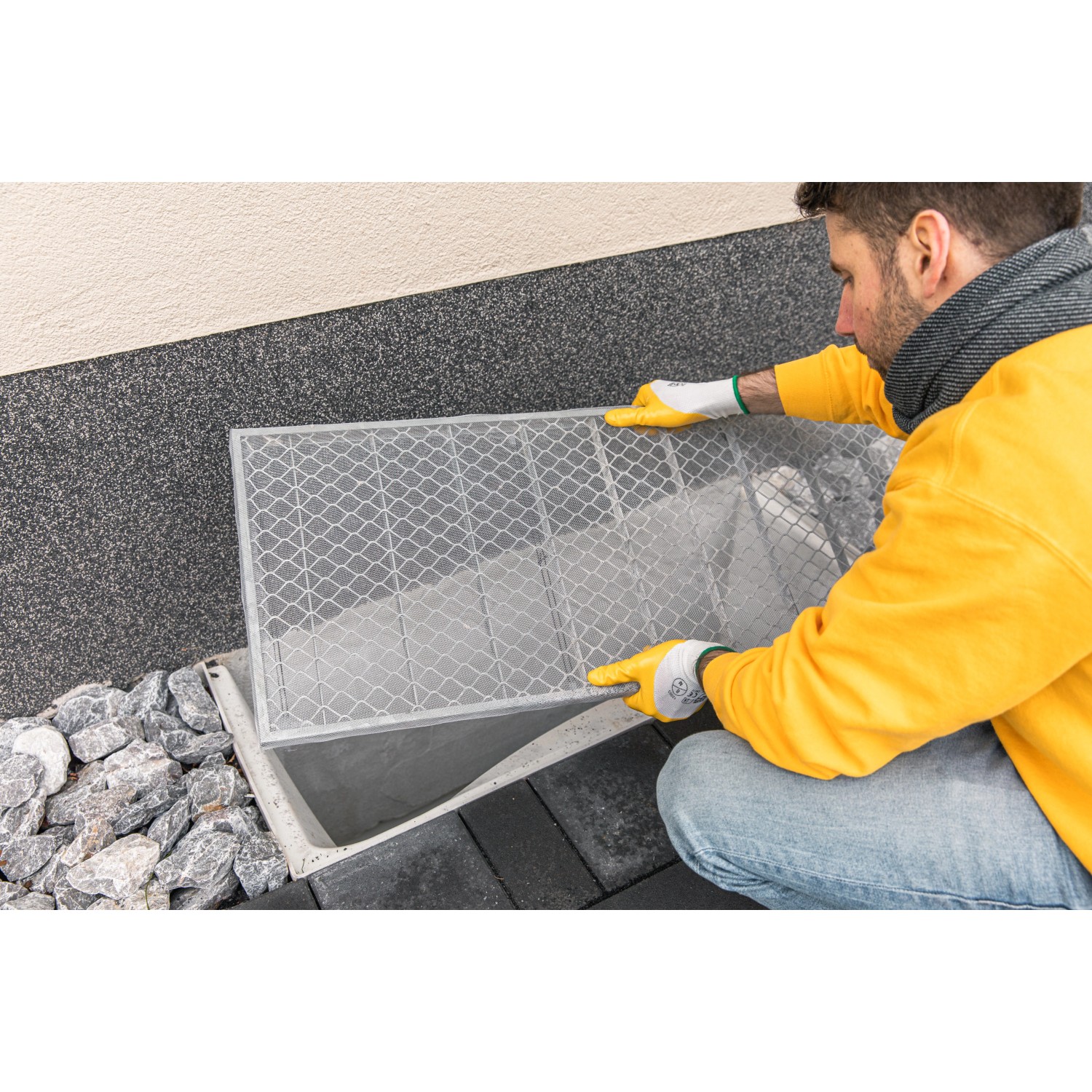 Mann montiert Schellenberg Lichtschachtabdeckung aus Aluminium (50x125cm) am Kellerschacht.