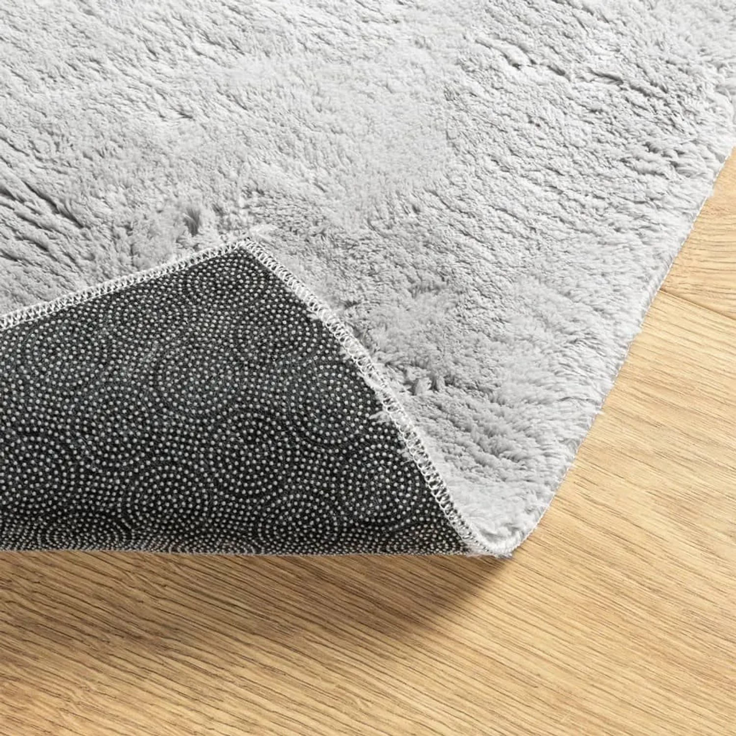 Grauer Kurzflor-Teppich HUARTE mit weicher Textur und schwarzer rutschfester Unterseite auf Holzfußboden.