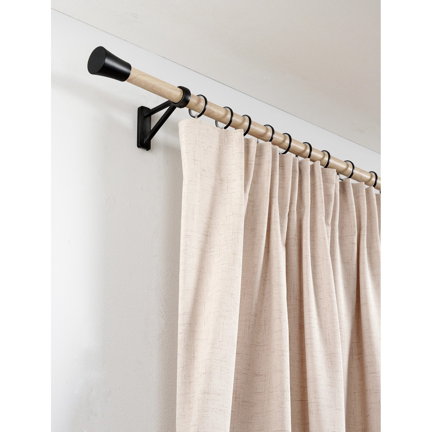 Gardinenstange mit Gardinenringen Denver, schwarz matt, und beigem Vorhang an weißer Wand.
