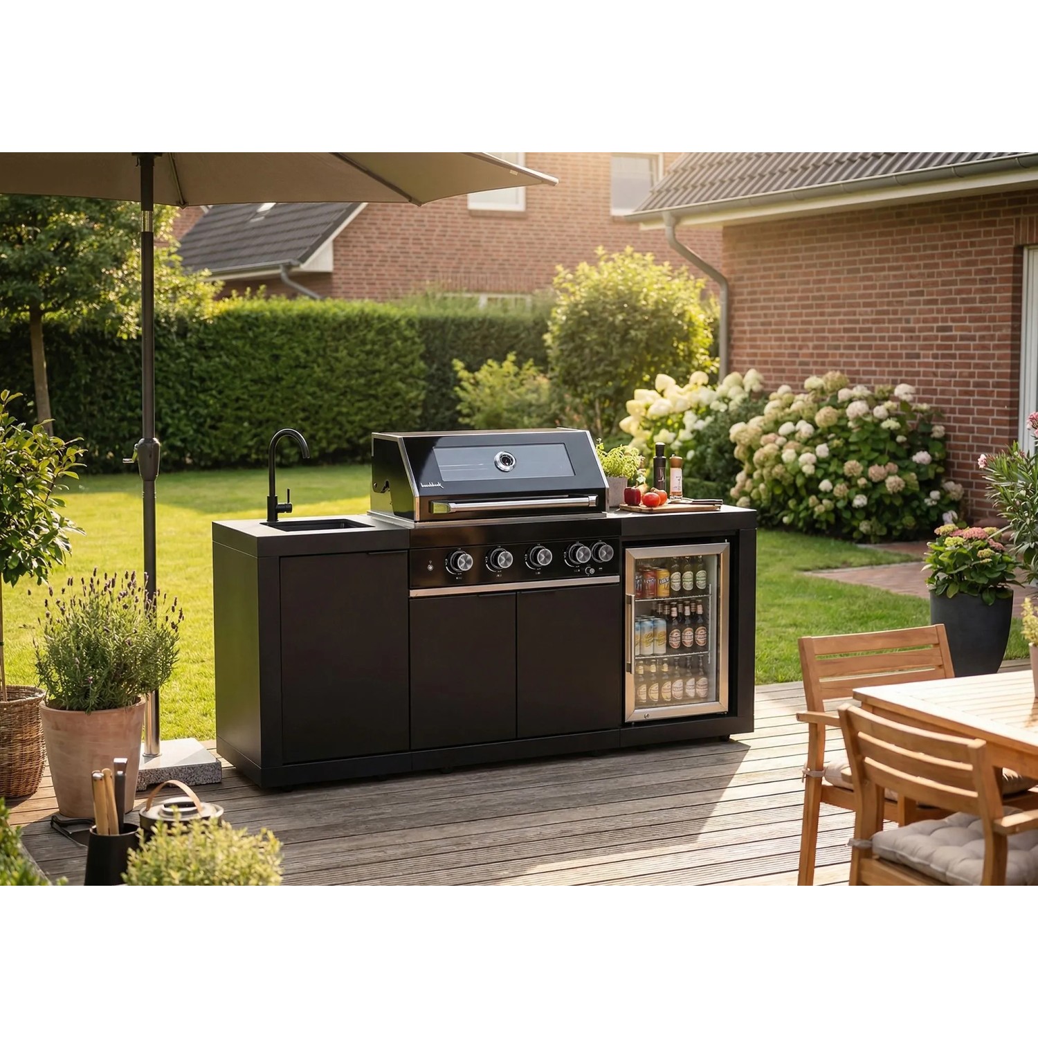 Buschbeck Outdoorküche Liverpool Schwarz mit Grill, Spüle und Kühlschrank im Garten.