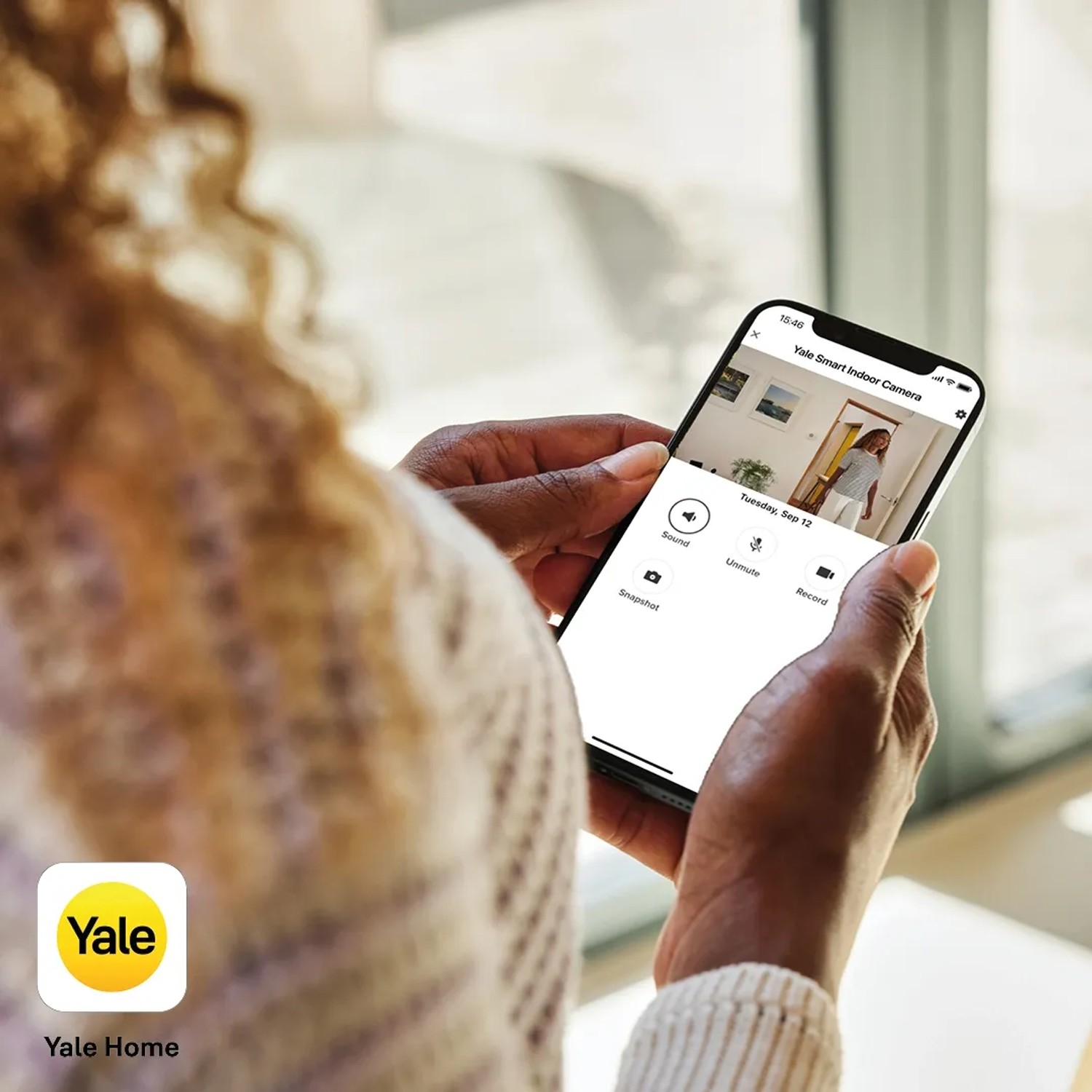 Frau bedient Yale Smart-Camera Innen WLAN Full HD Überwachungskamera per App auf Smartphone.