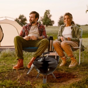 Schwarzer Relaxdays Kugelgrill aus Stahl mit Grillzange, tragbar, im Einsatz beim Camping mit Zelt.