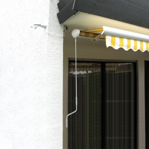Weiße Markisenkurbel (150cm) an einer gelb-weiß gestreiften Markise.