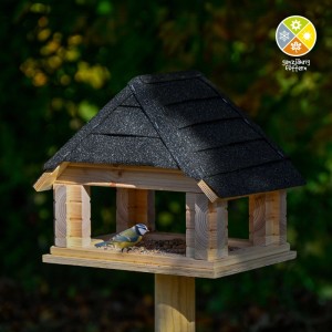 Dobar Vogelhaus Sort aus hellem Massivholz mit schwarzem Bitumendach; Blaumeise frisst am Futtertablett.