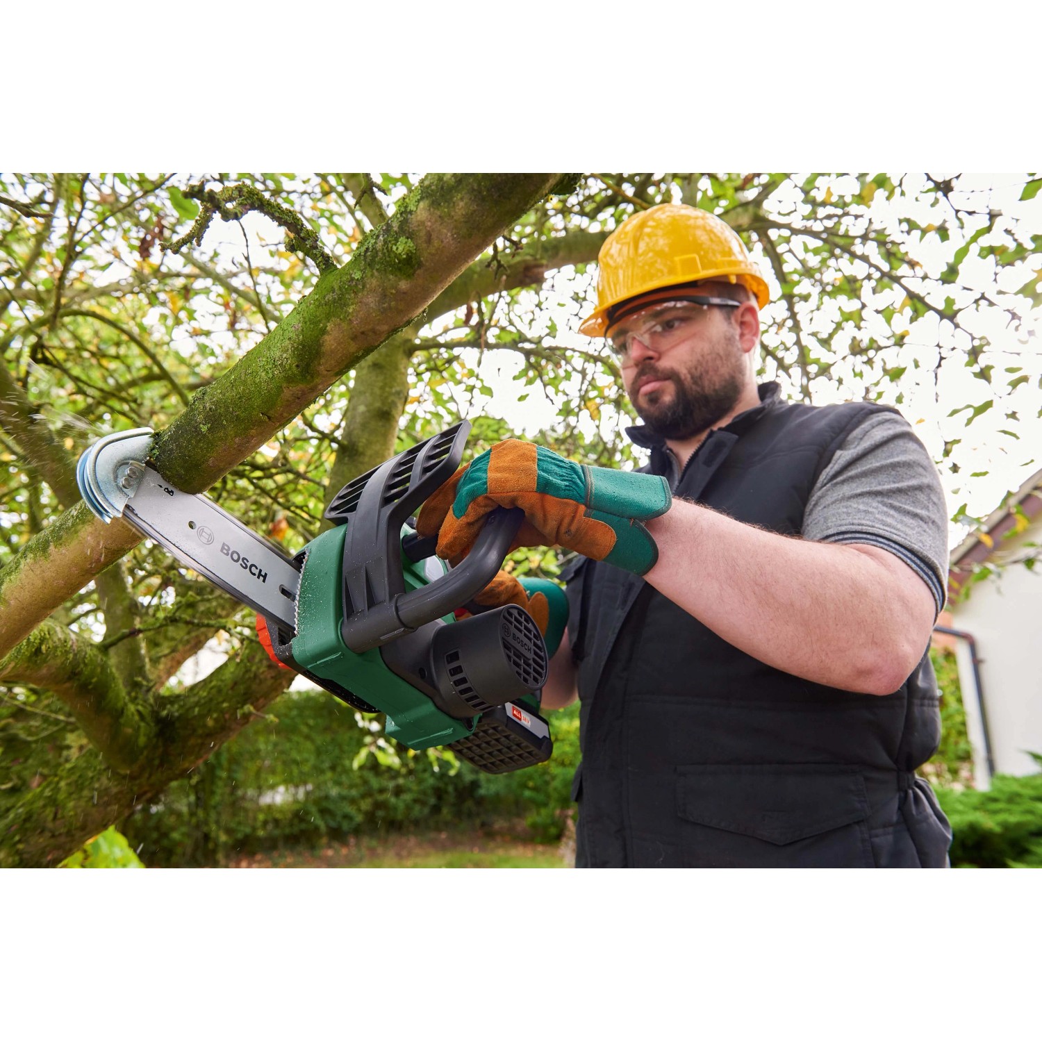 Mann sägt Ast mit Bosch Akku-Kettensäge UniversalChain 18. Kompakte Akku Kettensäge für Gartenarbeiten.