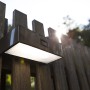 Moderne, eckige Lutec LED-Solar-Wandleuchte Brick aus Edelstahl an Holzzaun.