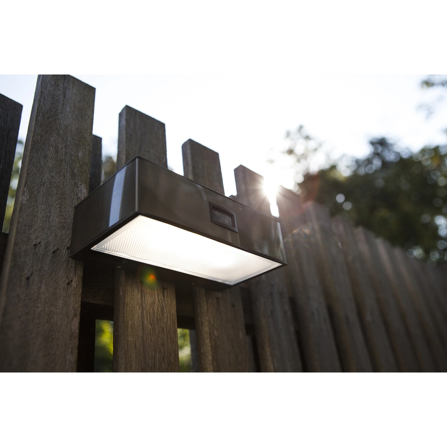 Moderne, eckige Lutec LED-Solar-Wandleuchte Brick aus Edelstahl an Holzzaun.