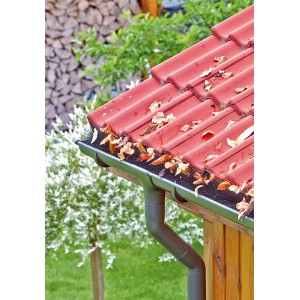 Verstopfte Dachrinne mit Laub unter rotem Ziegeldach. Marley Rinnenraupe schützt vor Verschmutzung.