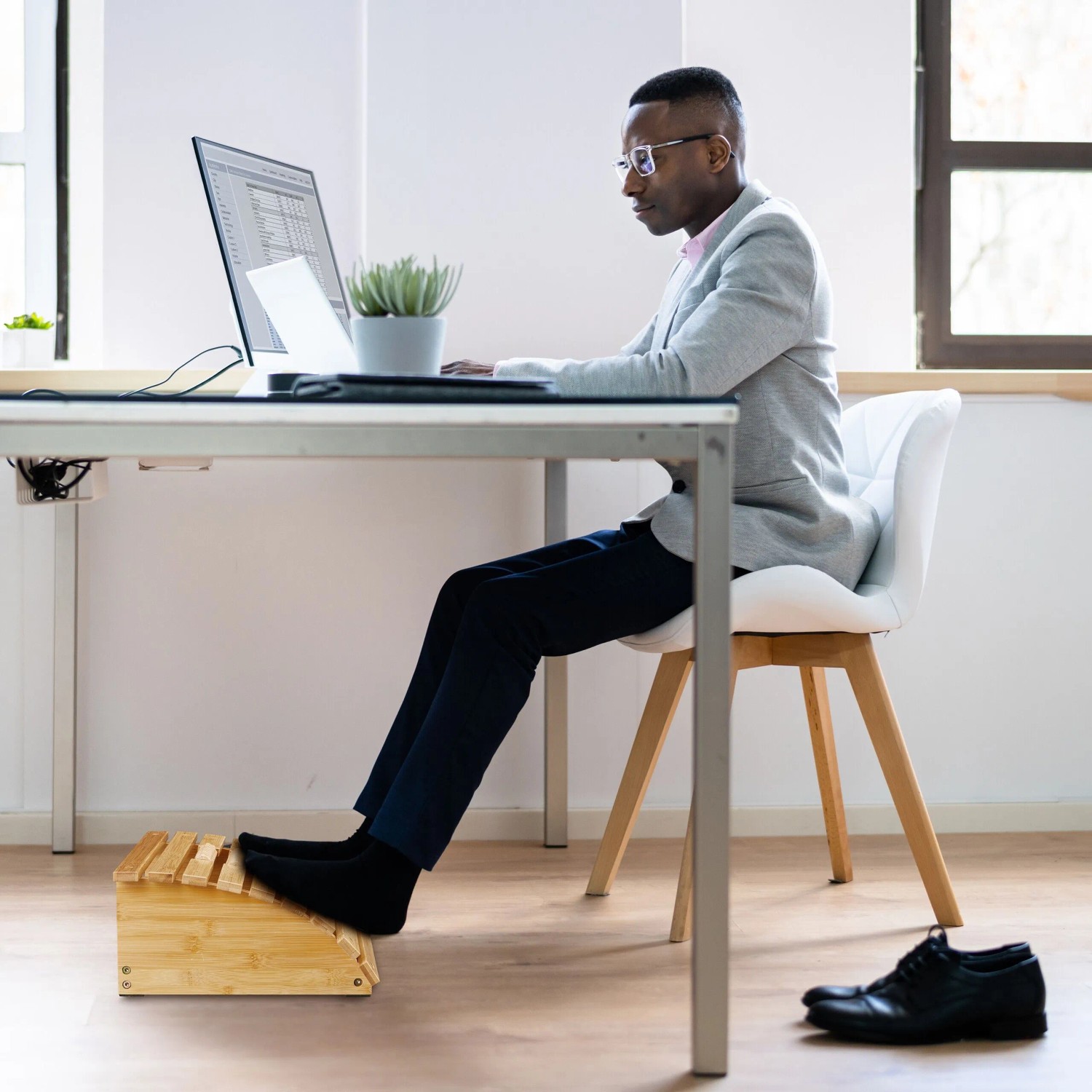 Mann nutzt Relaxdays Fußstütze aus Bambus unter Schreibtisch im Büro für bessere Haltung.