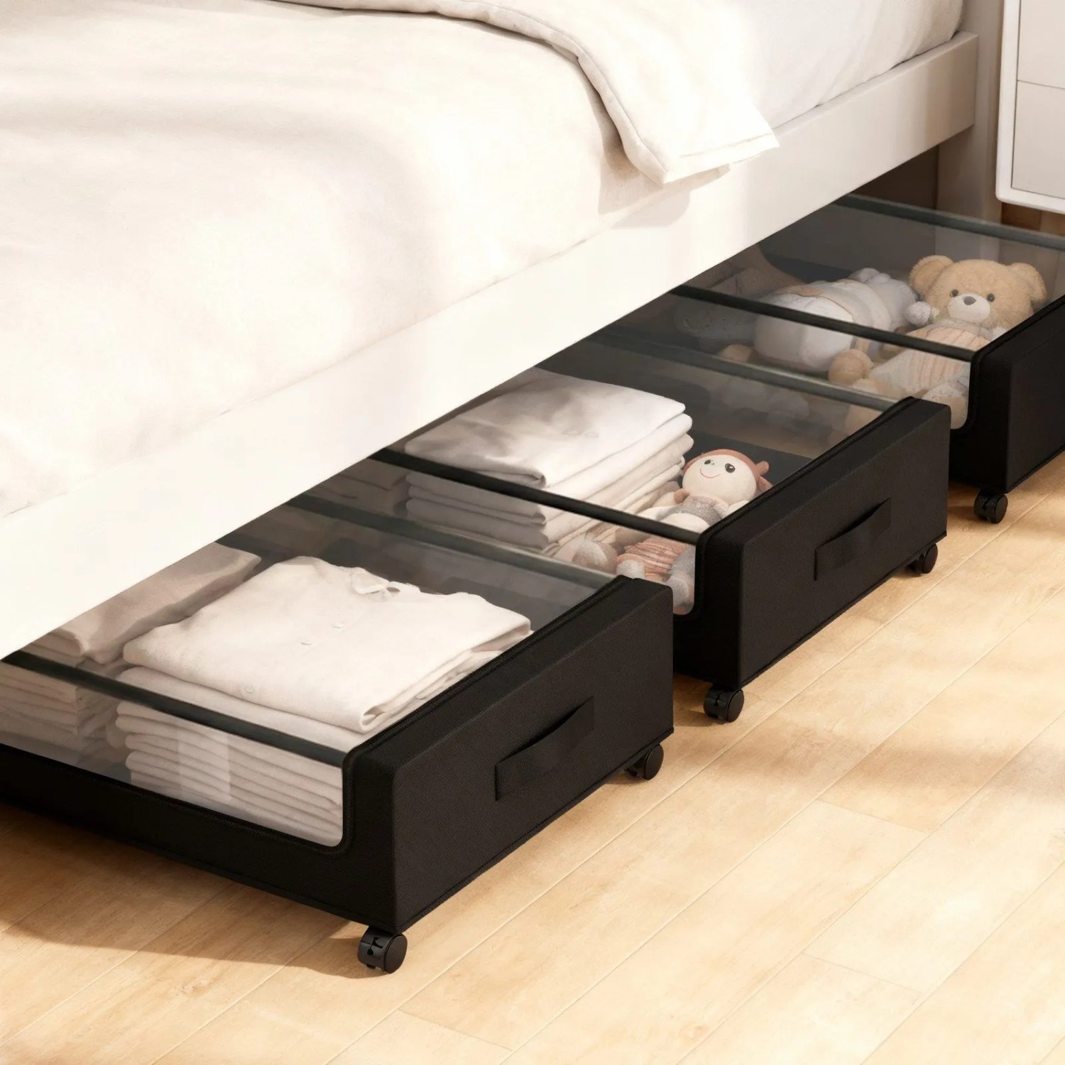 Drei schwarze Unterbett Aufbewahrungsboxen mit transparentem Deckel und Rollen unter einem Bett, gefüllt mit Textilien.