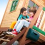 Axi Spielhaus Max mit Leiter, Rutsche und Sandkasten, zwei Kinder sitzen auf der Veranda.