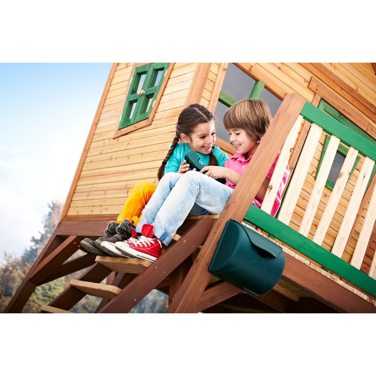 Axi Spielhaus Max mit Leiter, Rutsche und Sandkasten, zwei Kinder sitzen auf der Veranda.