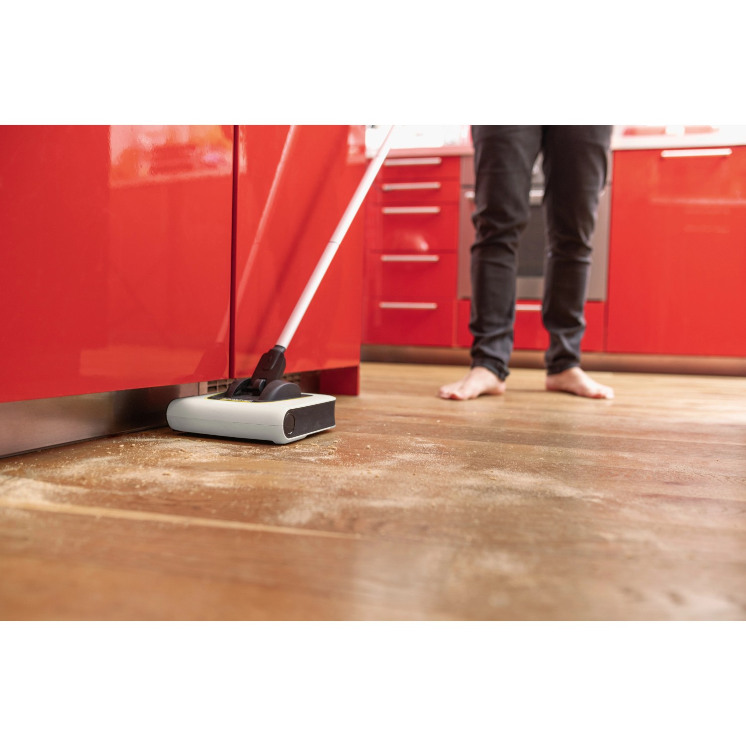 Kärcher Akku-Besen KB 5 im Einsatz auf Holzboden vor roter Küchenzeile.